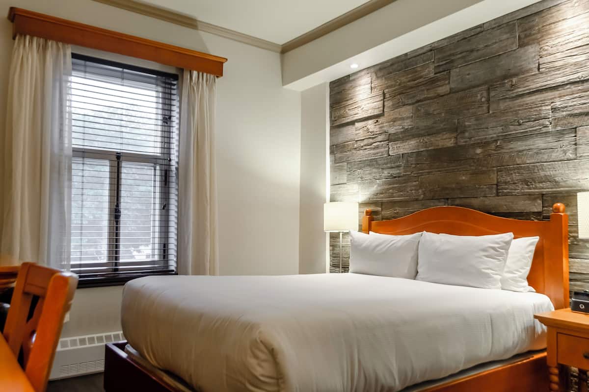 Una cama bien hecha con sábanas blancas, un cabecero de madera y una mesita de noche con lámpara.