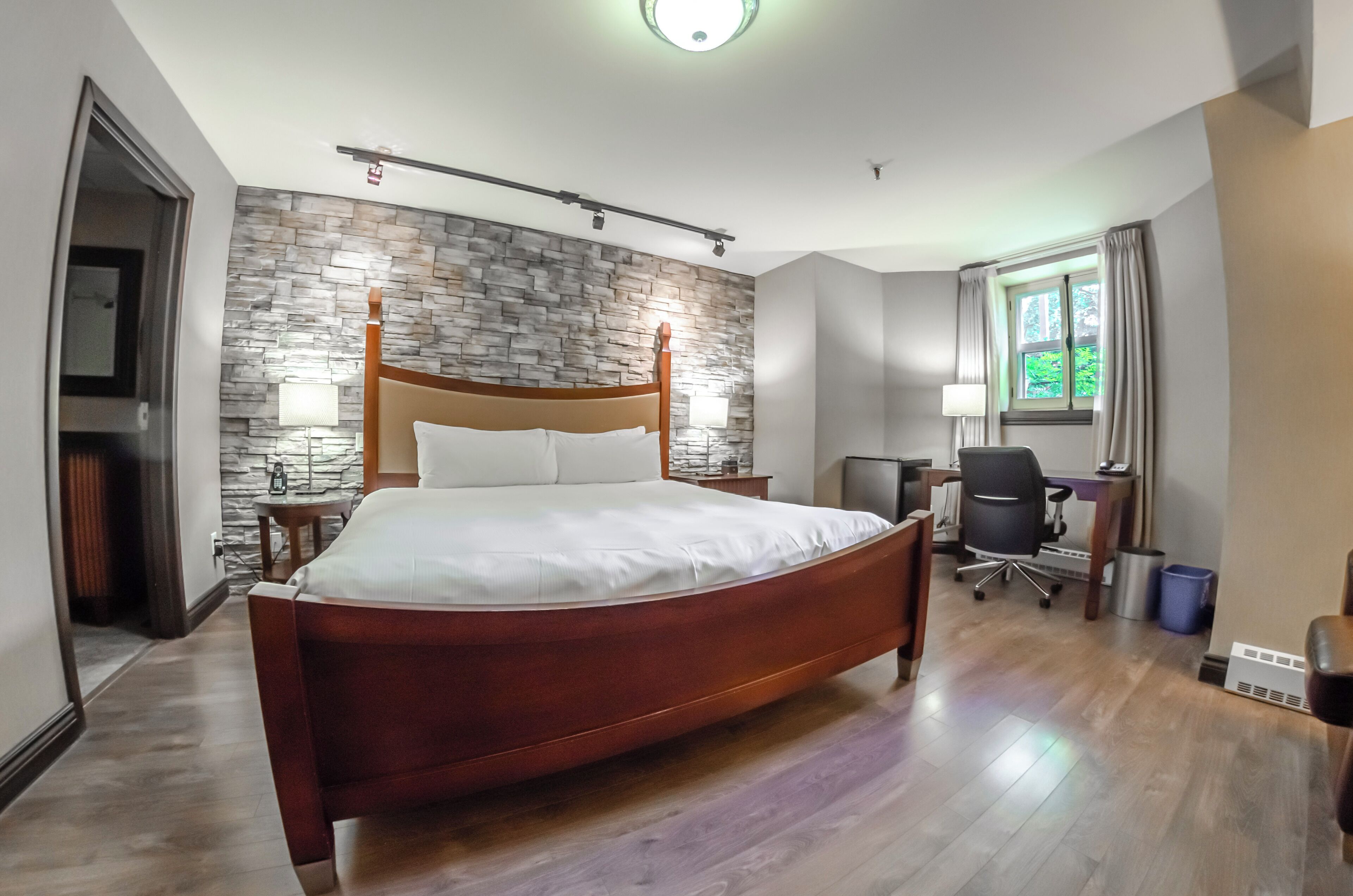 Una habitación de hotel moderna con una cama de madera, pared de piedra, escritorio y silla.