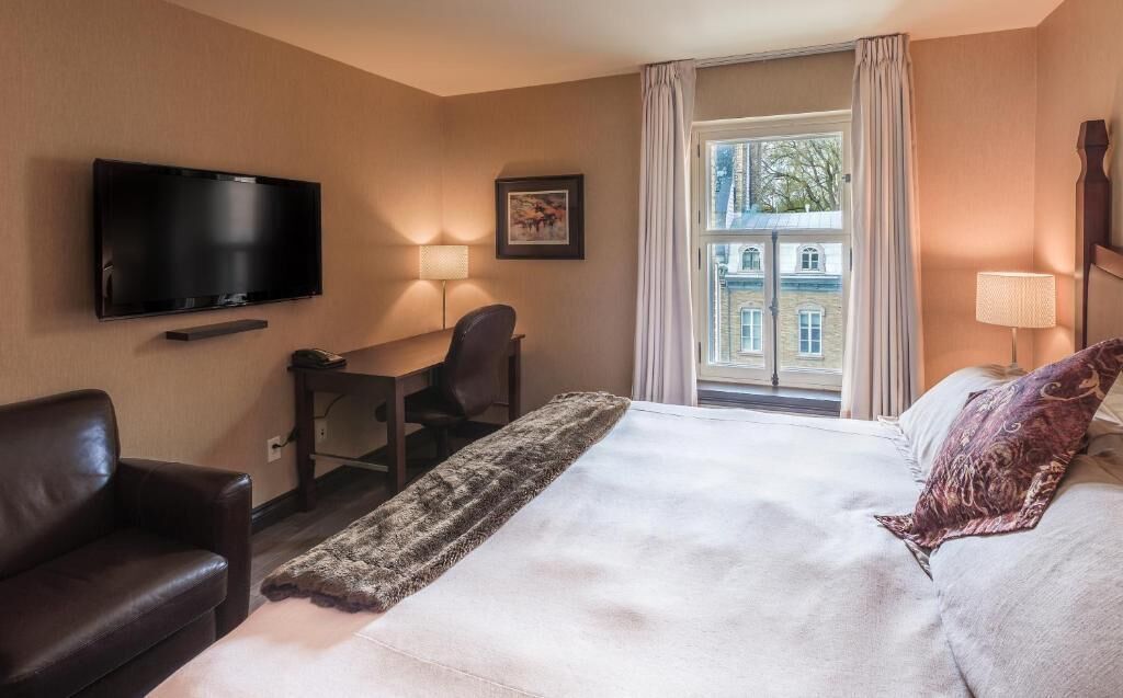 Habitación de hotel con cama, escritorio, silla, televisión y ventana con cortinas.