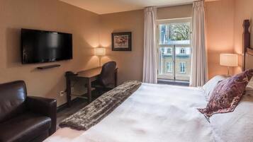 Habitación de hotel con cama, escritorio, silla, televisión y ventana con cortinas.