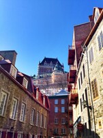 Un edificio histórico con torreta y tejado rojo, rodeado de edificios de piedra con múltiples ventanas y balcones.