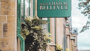A green sign for Hôtel Château Bellevue with a classic architectural style.