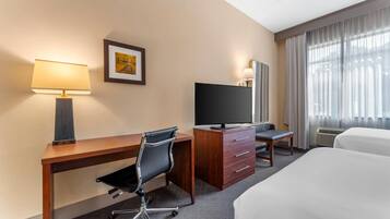 Une chambre d’hôtel avec un bureau en bois, un fauteuil de bureau noir, une télévision, un lit et une fenêtre avec des rideaux.