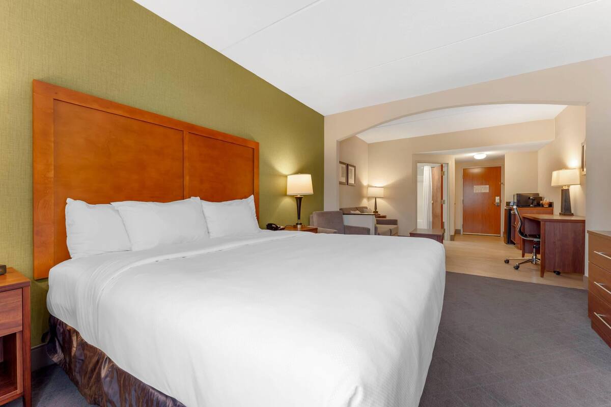 Una habitación de hotel con una cama grande, un escritorio, una silla y un aparador.