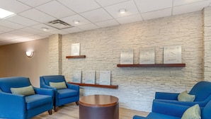 A lobby with blue armchairs, a round table, and a stone wall with framed awards. - Comfort Inn & Suites LaVale - Cumberland (Cumberland)