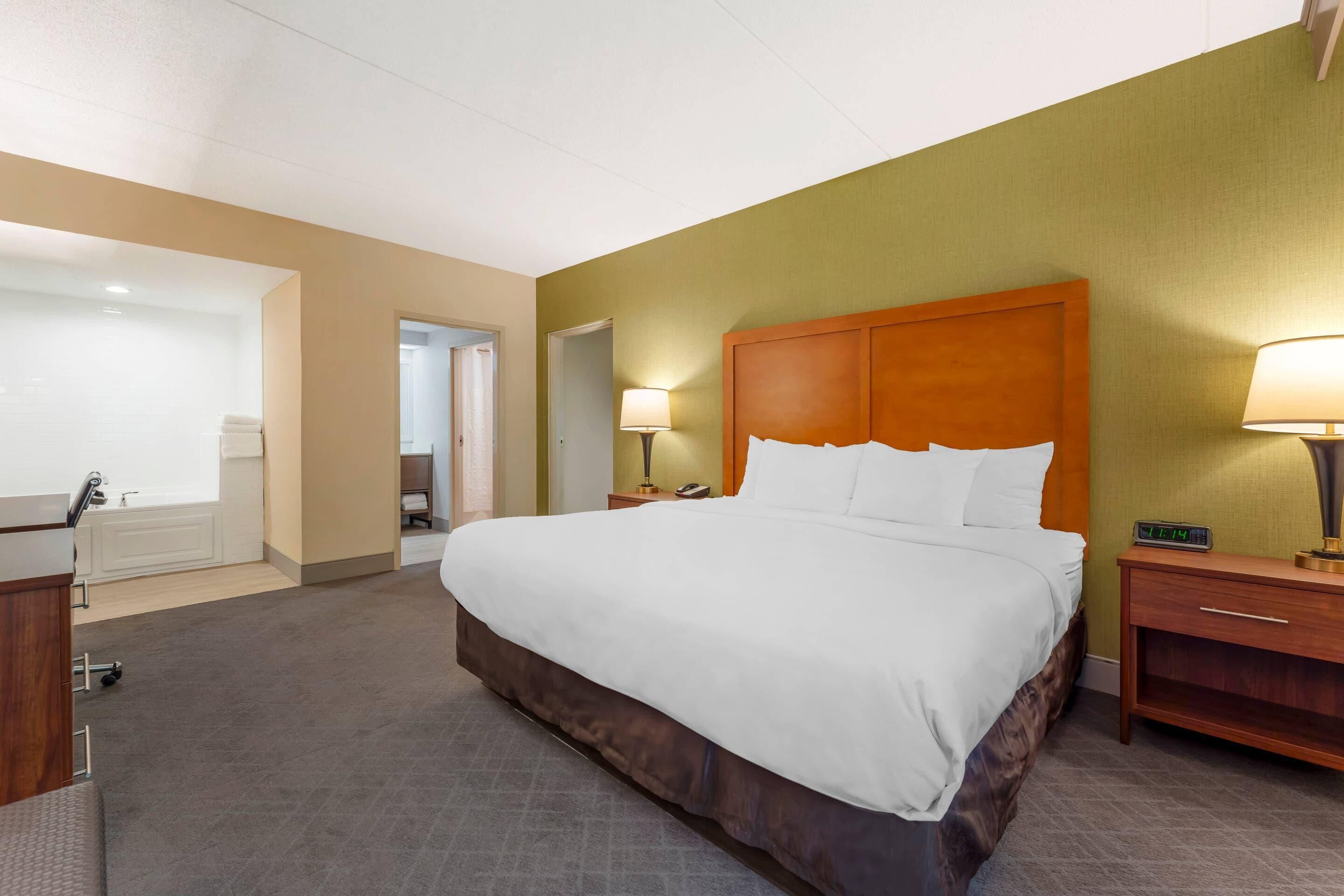 Habitación de hotel con una cama grande, un escritorio, una silla, una mesita de noche con lámpara y un espejo.