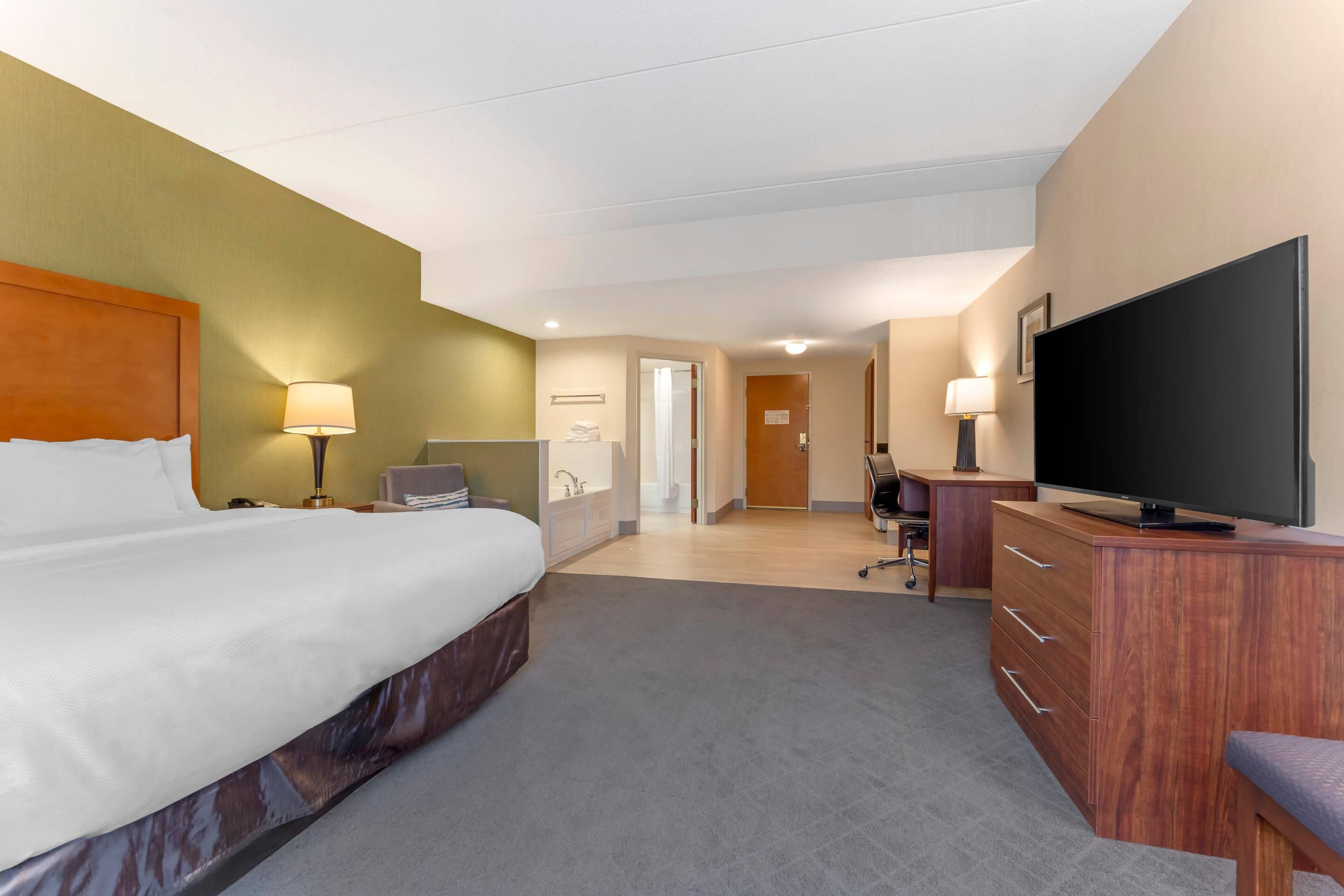 Une chambre d’hôtel avec un lit, un bureau, une télévision et une salle de bain que l’on aperçoit à l’arrière-plan.