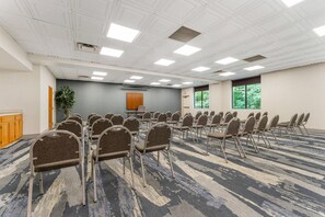 A conference room with rows of chairs, a podium, and a large window with a view of trees. - Comfort Inn & Suites LaVale - Cumberland (Cumberland)
