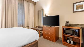 Habitación de hotel con cama, televisión, cómoda de madera, microondas y un cuadro en la pared.