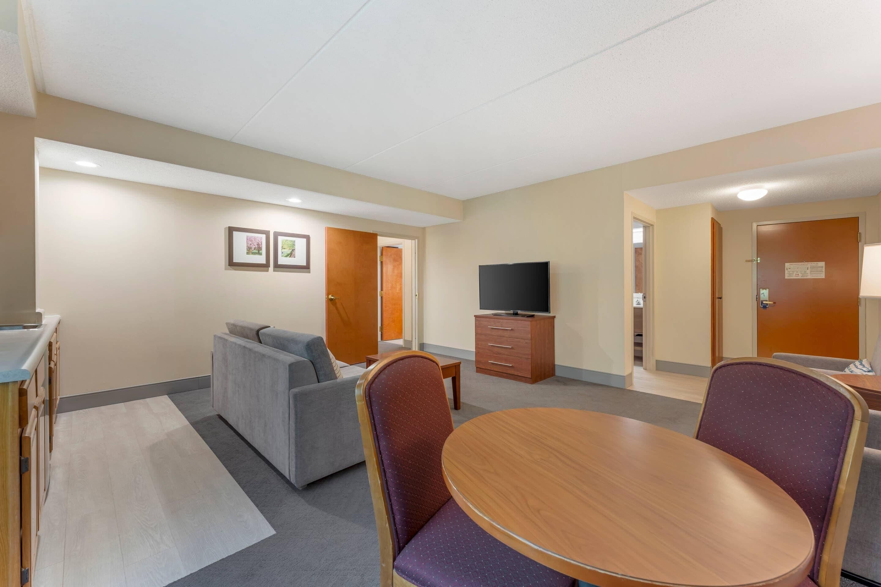 A hotel room with a sofa, a dining table, a TV, and a cabinet.