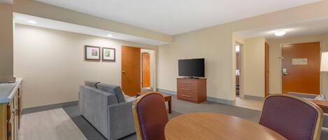 A hotel room with a sofa, a dining table, a TV, and a cabinet.