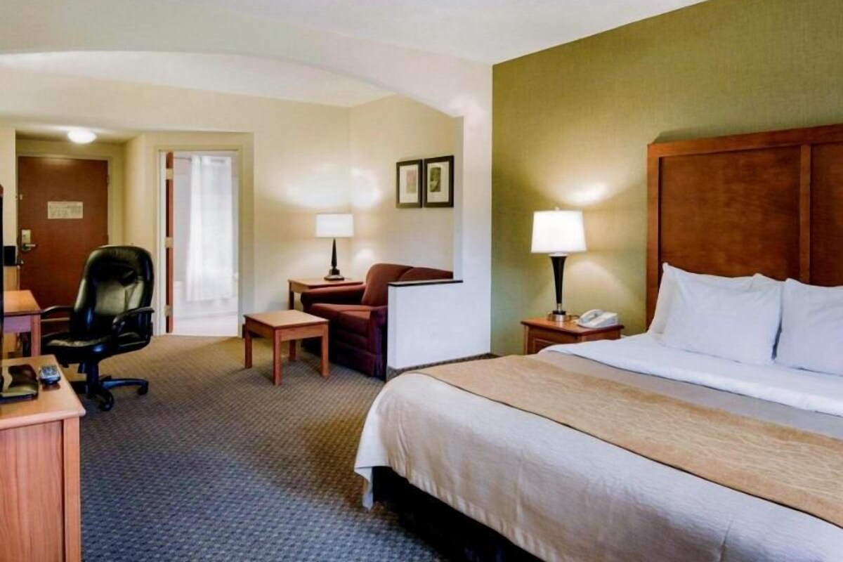 A hotel room with a bed, desk, chair, and two bedside tables with lamps.