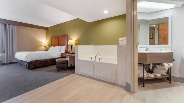 A hotel room with a bed, a sitting area, a large bathtub, and a vanity with a mirror. - Comfort Inn & Suites LaVale - Cumberland (Cumberland)