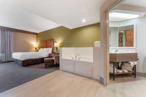 A hotel room with a bed, a sitting area, a large bathtub, and a vanity with a mirror.