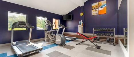 A gym with treadmills, an elliptical, a rowing machine, and dumbbells.
