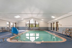 An indoor swimming pool with clear blue water, a covered chair, and a large window.