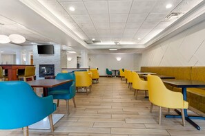A modern restaurant with wooden flooring, yellow and blue chairs, and a flat-screen TV mounted on the wall.