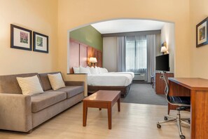 Ein Hotelzimmer mit einer Couch, einem Bett, einem Schreibtisch, einem Fernseher und einer Lampe.