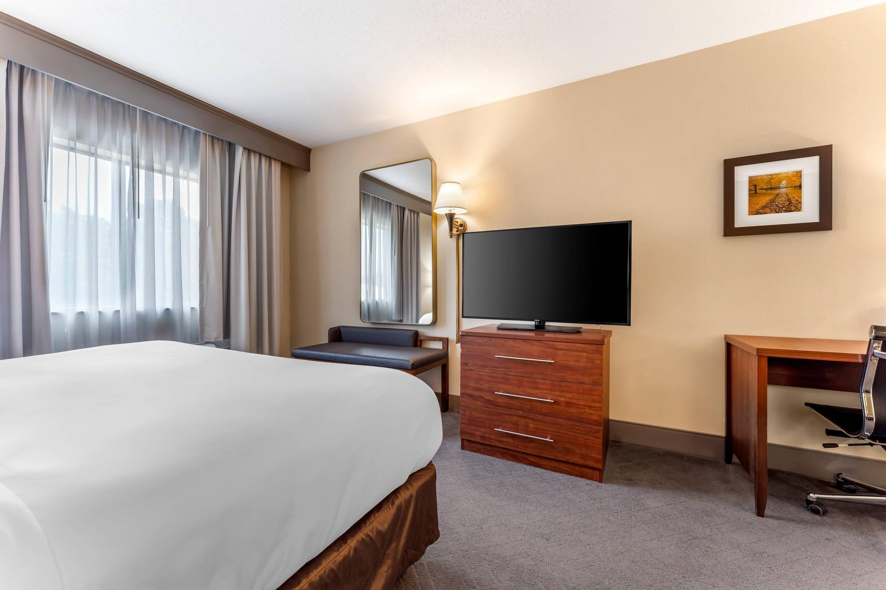 A hotel room with a bed, a desk, a television, a dresser, and a framed picture on the wall.
