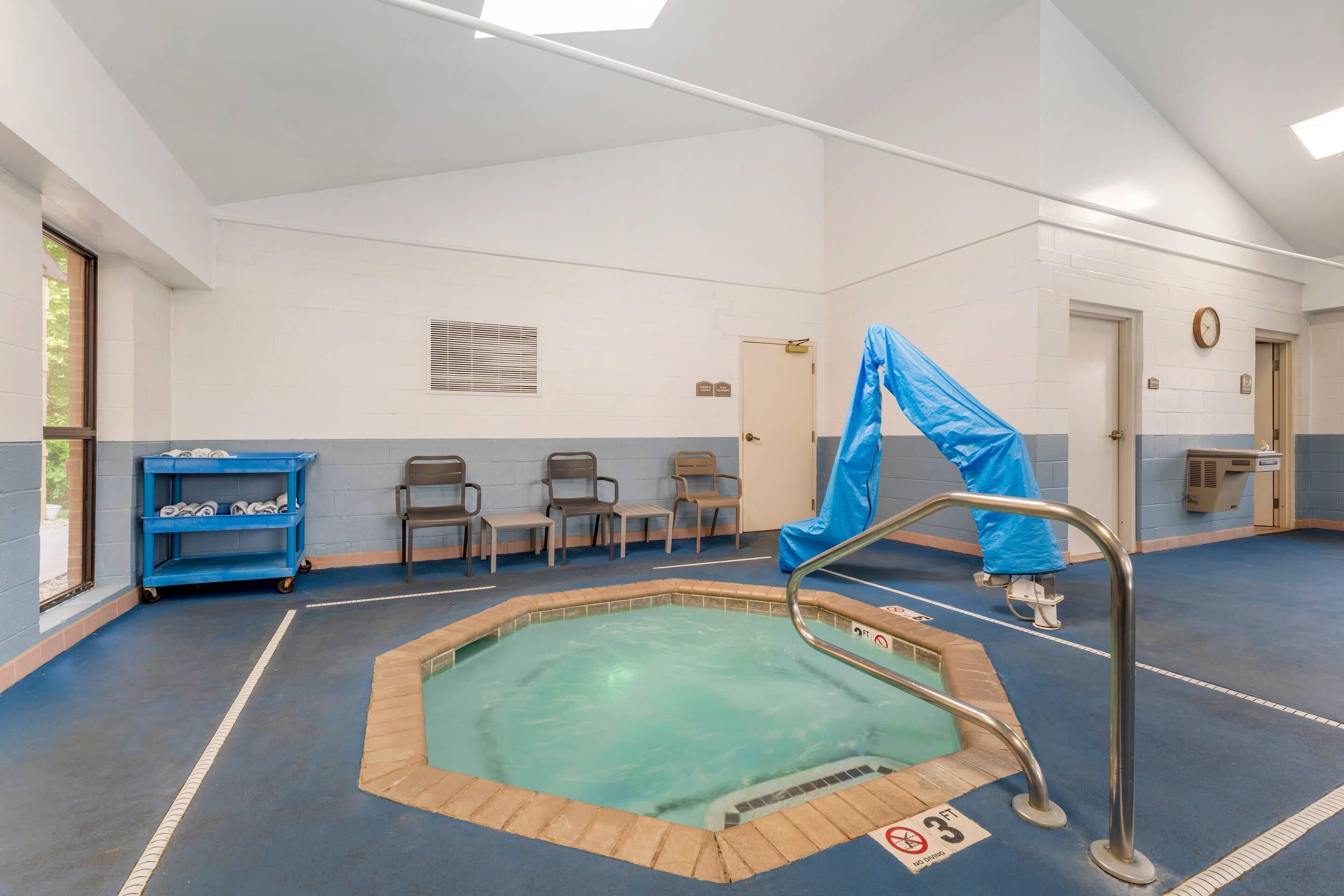 Un espace piscine avec une bâche bleue, un escalier métallique pour piscine et un chariot bleu contenant des serviettes.