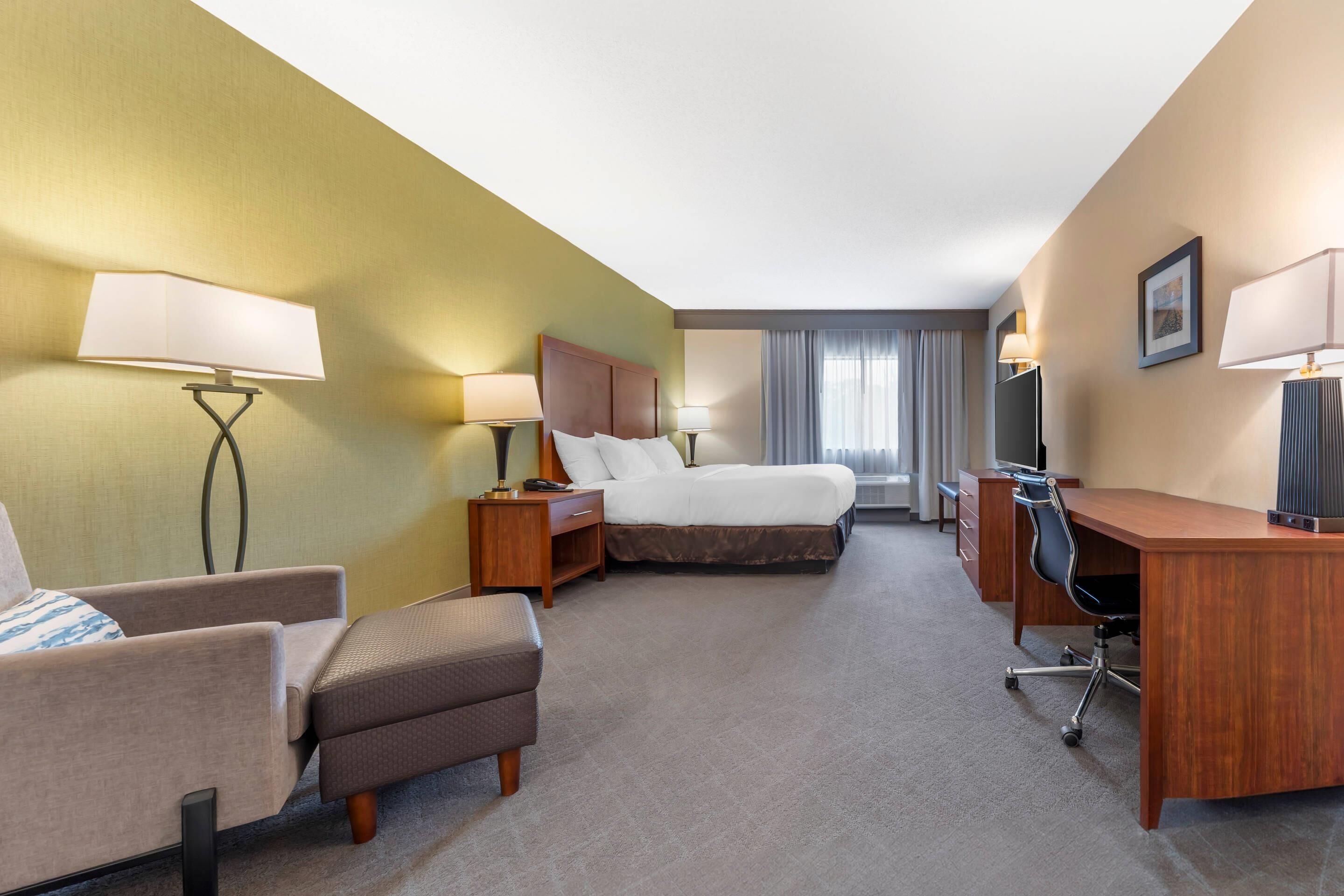 A hotel room with a bed, a desk, a chair, a sofa, and a lamp.