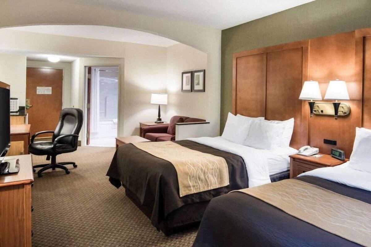 A hotel room with two beds, a desk, a chair, a lamp, and a television.
