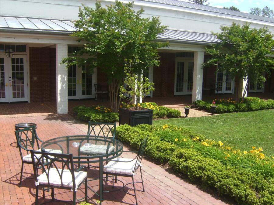 A patio with a round table and chairs, surrounded by a brick pathway and greenery.