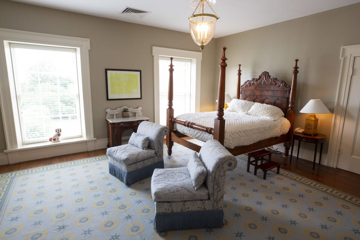 A bedroom with a four-poster bed, two armchairs, a small table, and a lamp.