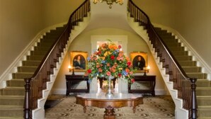 Una imponente escalera con un candelabro, un centro de mesa floral y un suelo con diseño.