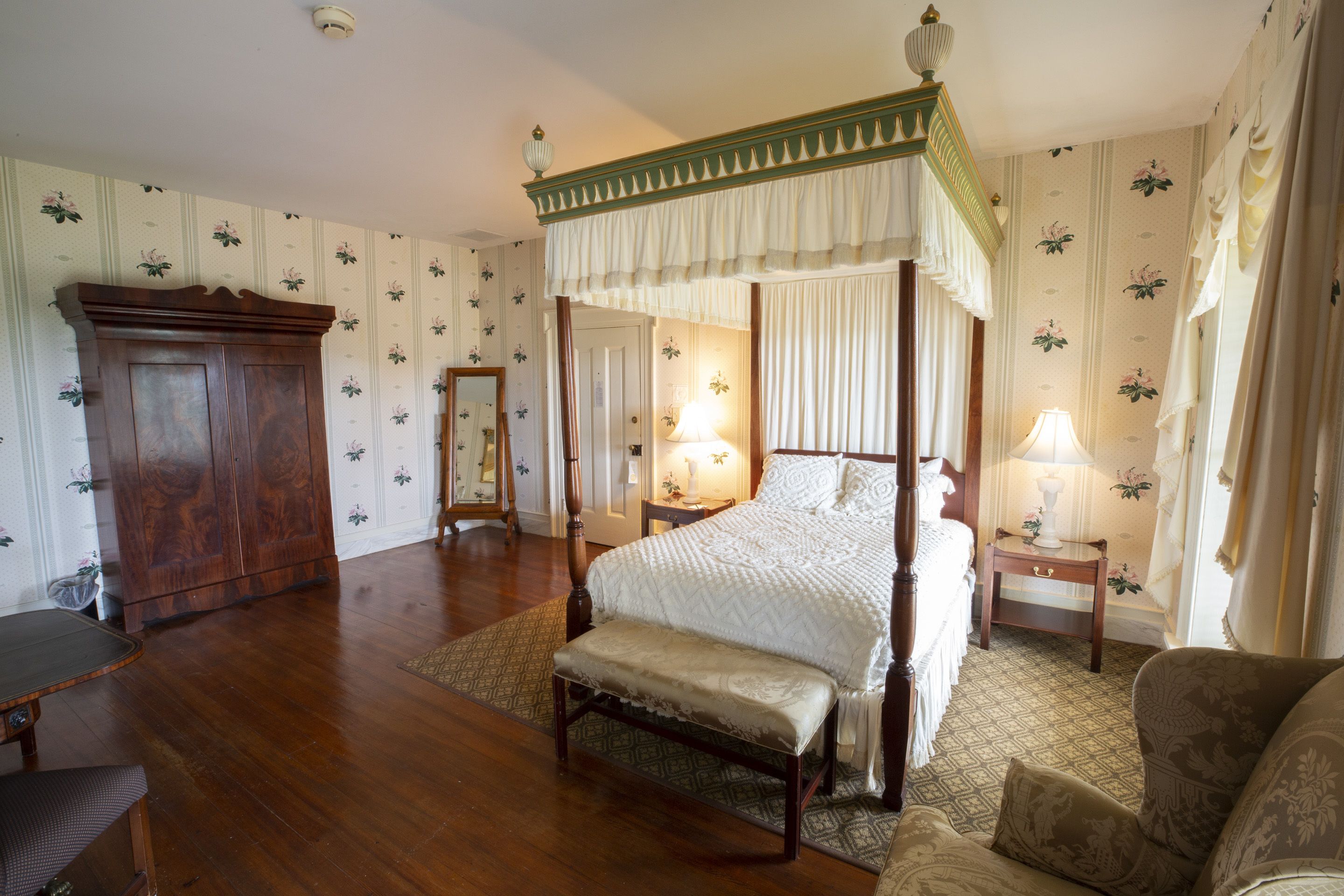 Un lit à baldaquin, une armoire en bois, un banc, une table de chevet avec une lampe et un tapis à motifs.