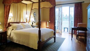 A four-poster bed with a canopy, a nightstand with a lamp, a chair, and a desk with drawers. - The Berry Hill Resort & Conference Center (South Boston)