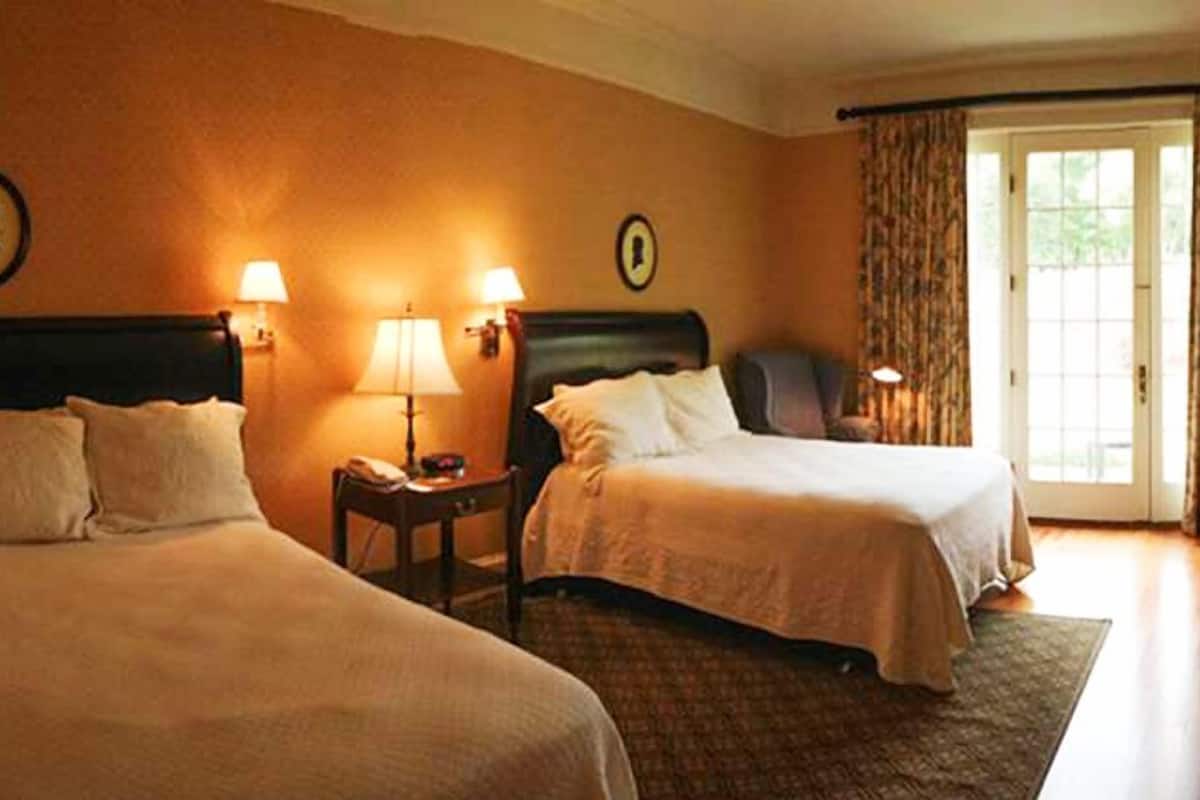 A hotel room with two beds, a small table, and lamps.