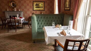 A dining area with a green upholstered booth, a white table with a menu, and a fireplace.