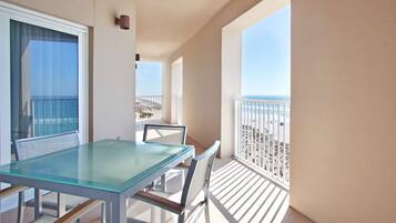 A balcony with a glass table and chairs, a view of the beach, and a railing.