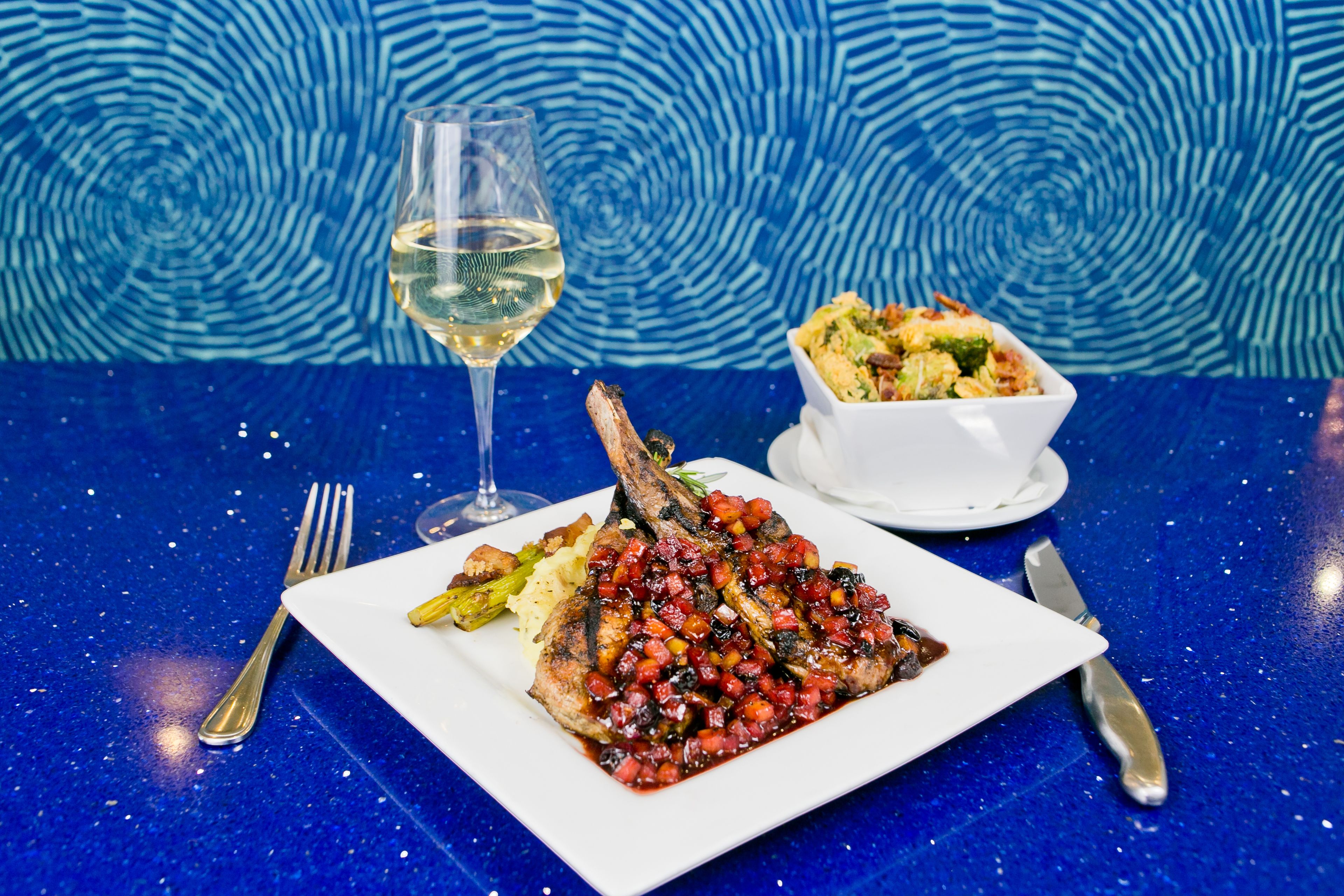 A plate of food with a glass of white wine on a table with a blue patterned background.