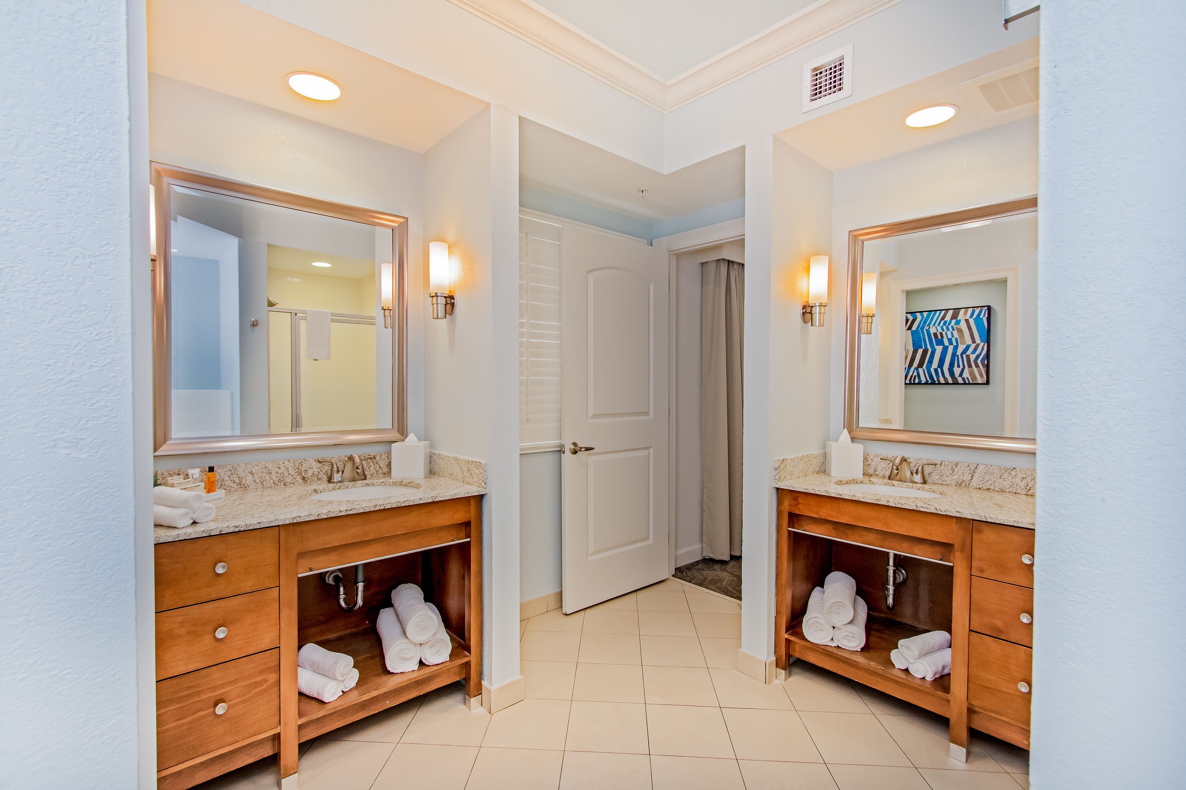 A hotel bathroom with two sinks, wooden vanity, towel storage, and a mirror.