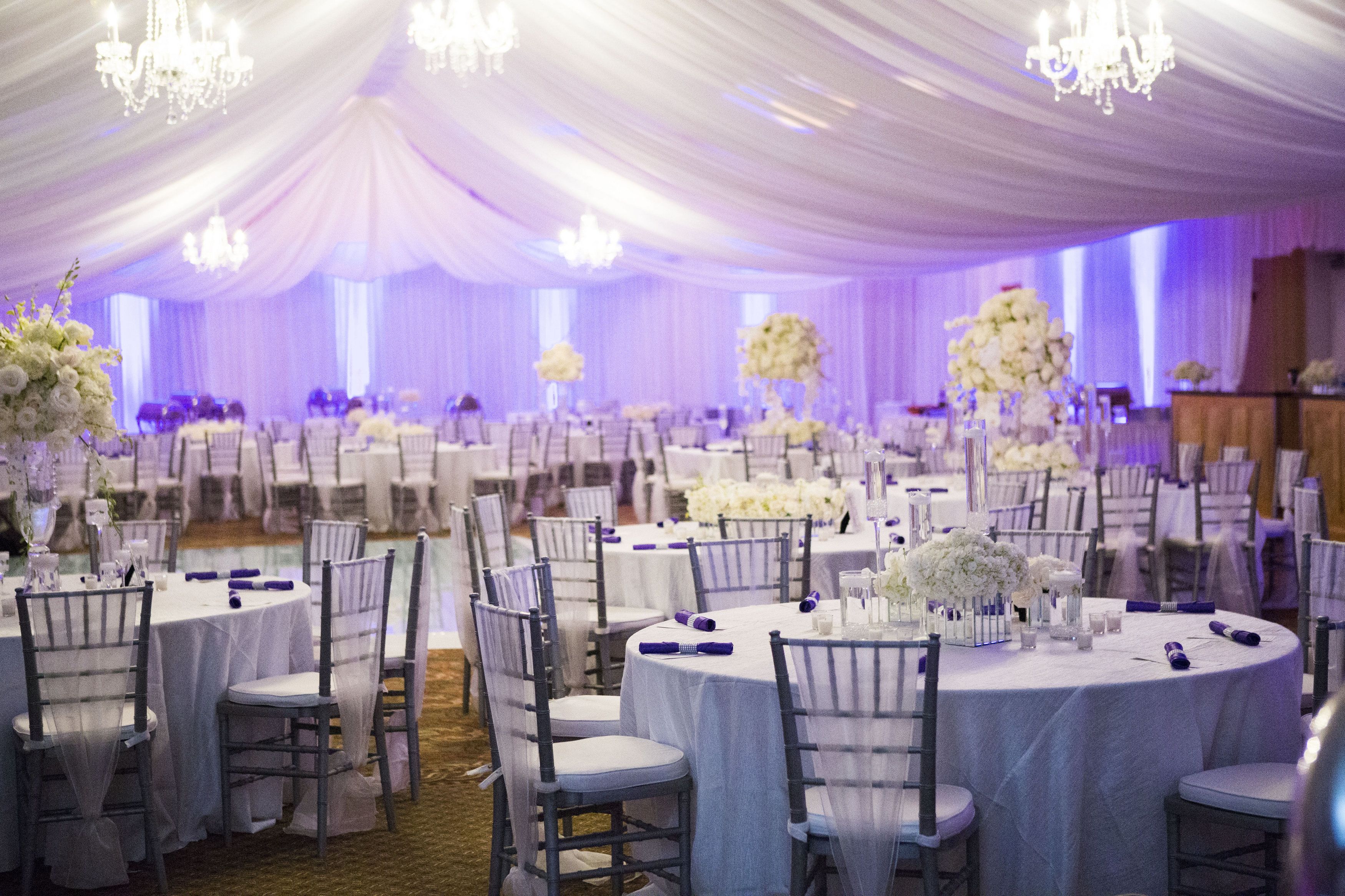 A banquet hall with round tables, white chairs, and floral centerpieces.
