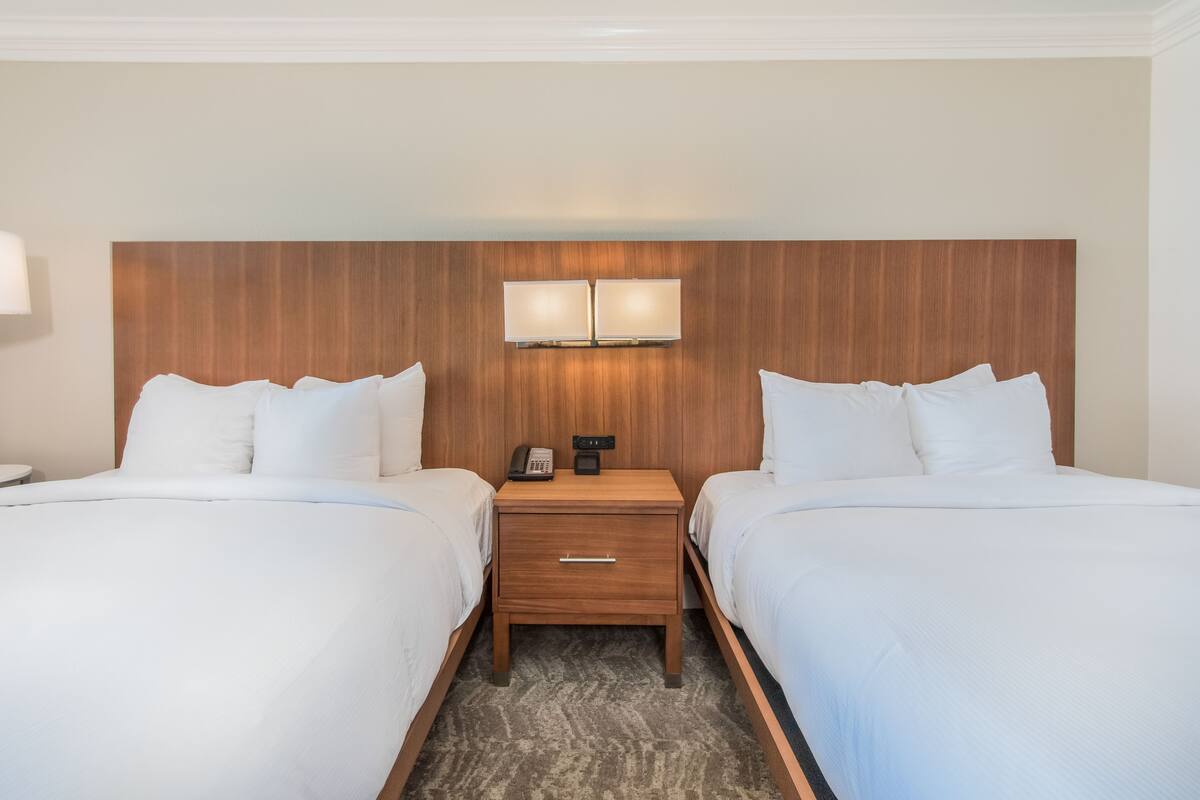 Une chambre d’hôtel avec deux lits, une tête de lit en bois, une table de chevet avec une lampe et un téléphone.