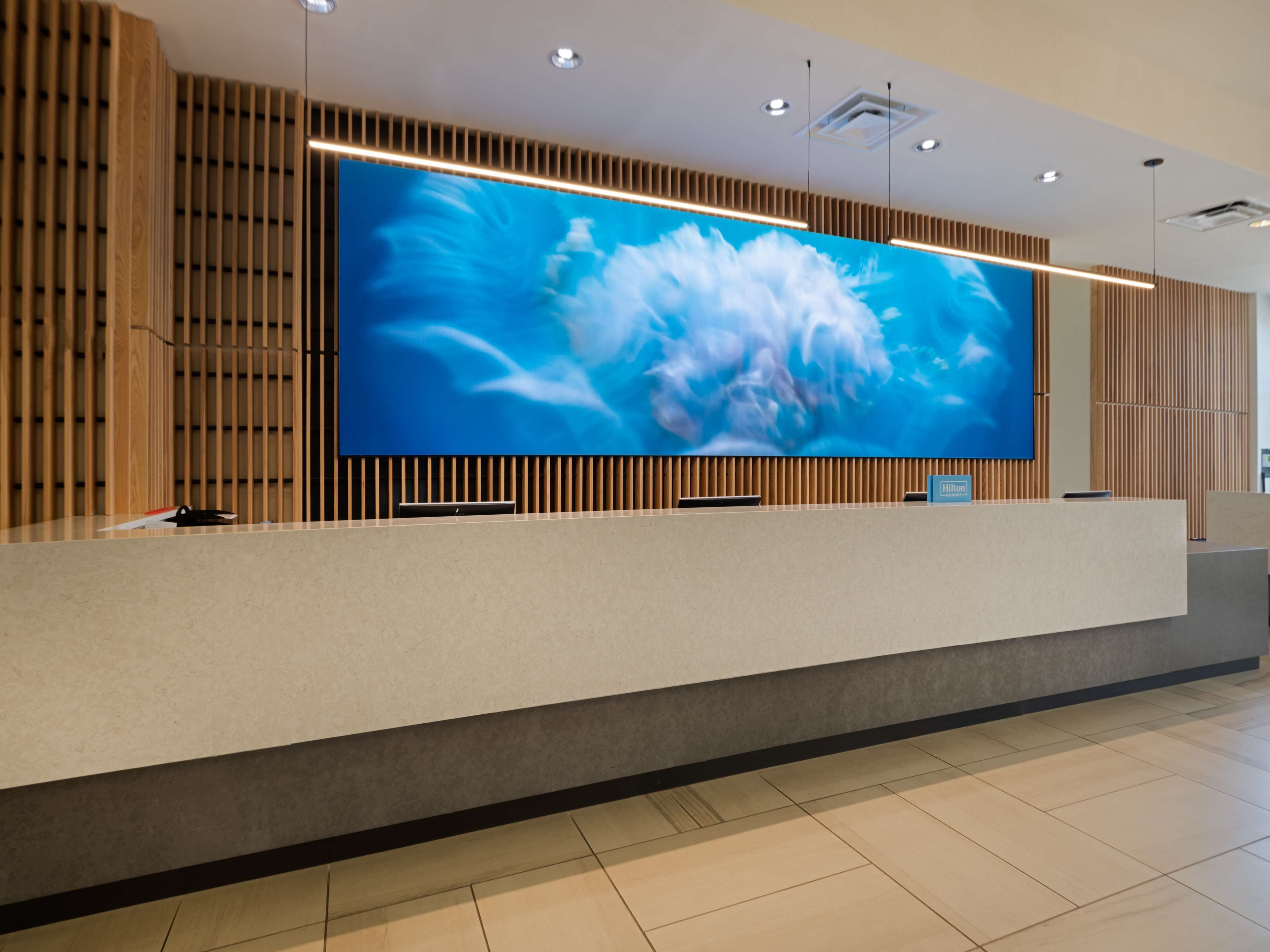 Een modern receptiebalie met een groot flatscreen-televisie waarop een bloemenafbeelding wordt getoond, houten lambrisering aan de wanden en een schoon, minimalistisch design.