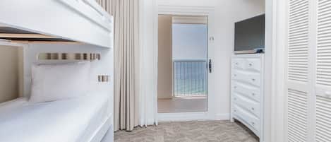 A hotel room with a bunk bed, a walk-in closet, a television, and a door leading to a balcony.