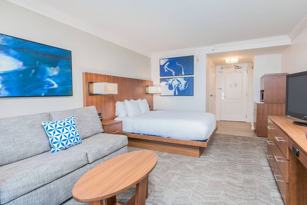 Une chambre d’hôtel moderne équipée d’un lit, d’un canapé, d’une télévision et ornée d’œuvres d’art sur les murs.
