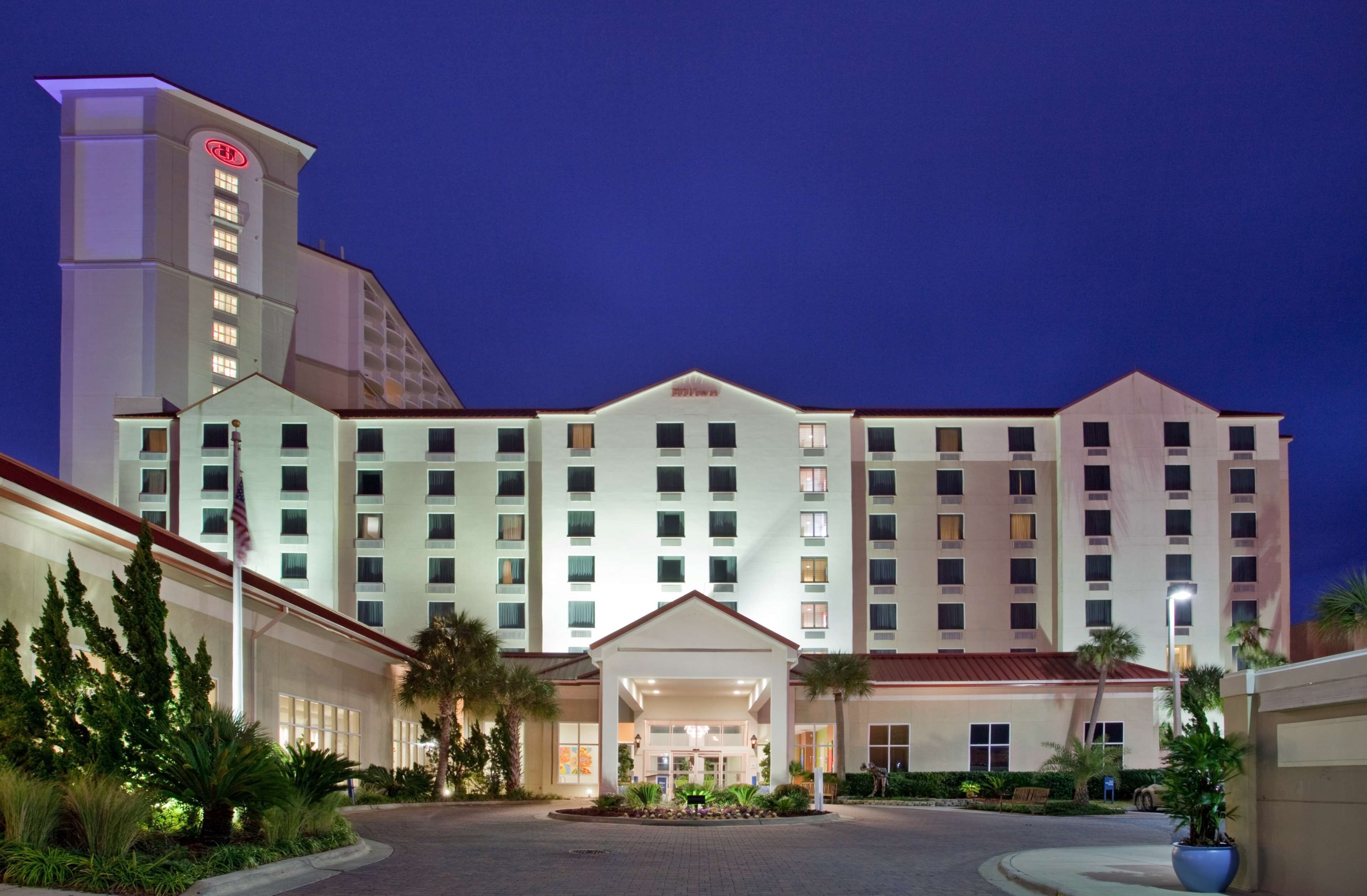 A multi-story hotel with a central entrance, a flagpole, and a well-lit facade.