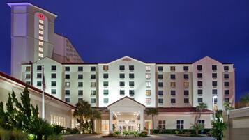 A multi-story hotel with a central entrance, a flagpole, and a well-lit facade.
