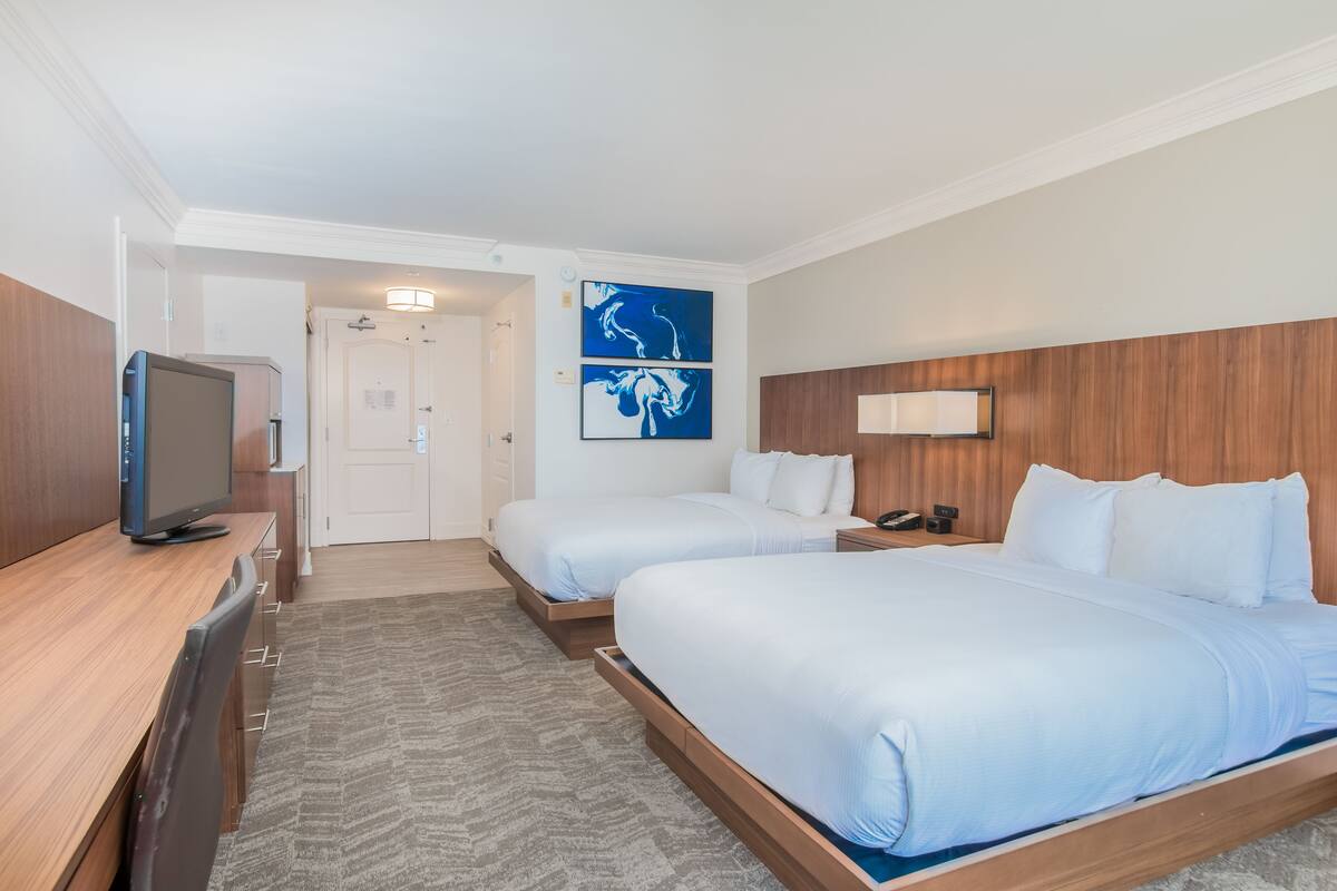 Une chambre d’hôtel avec deux lits, une télévision, un bureau et des œuvres d’art accrochées au mur.