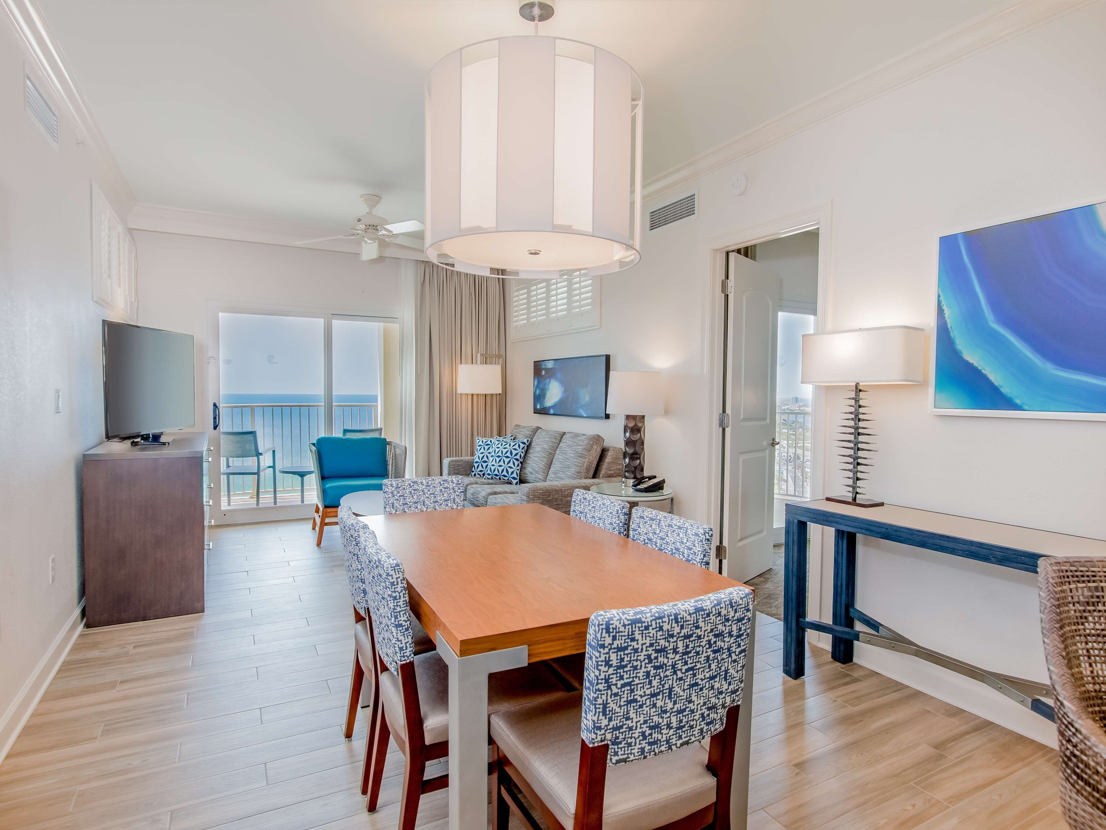 A modern dining area with a wooden table and patterned chairs, a ceiling fan, and a view of the balcony.