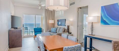 A modern dining area with a wooden table and patterned chairs, a ceiling fan, and a view of the balcony.
