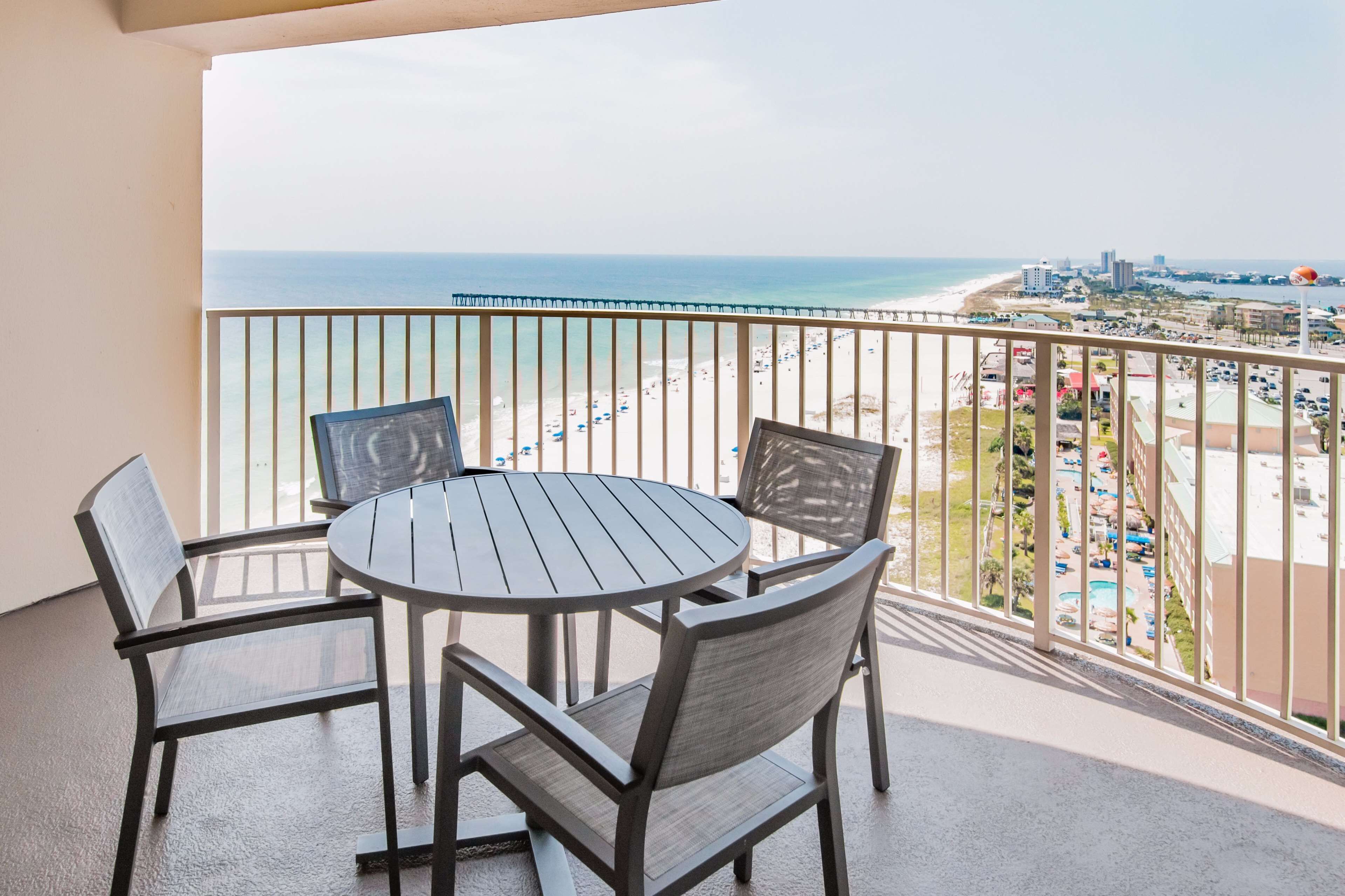 A balcony with a round table and four chairs, overlooking a beach and cityscape.