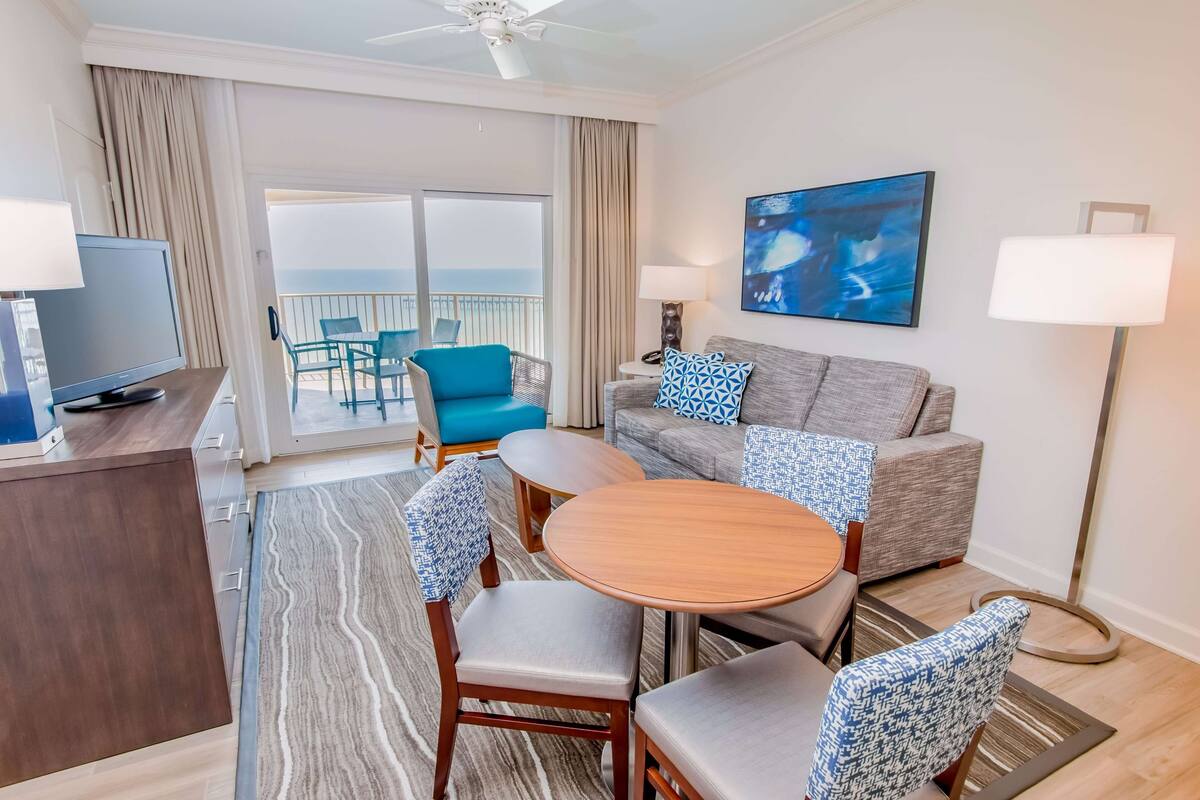 Une chambre d’hôtel avec un balcon, un canapé, une table basse et un téléviseur.