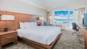Une chambre d’hôtel dotée d’un grand lit, de tables de chevet, d’un bureau avec une chaise, d’une télévision et offrant une vue sur l’océan depuis une porte-fenêtre donnant sur un balcon.