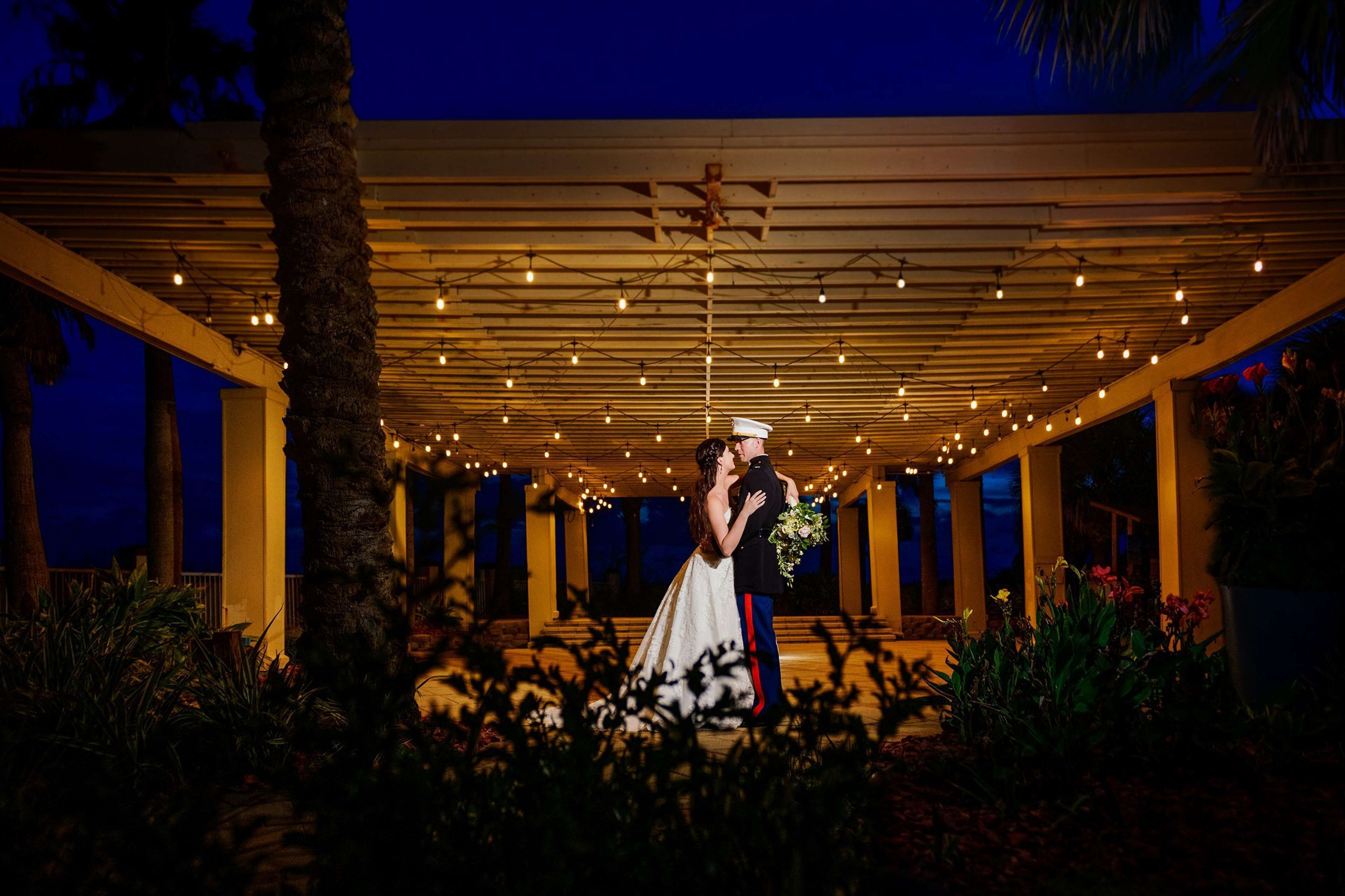 A couple embracing under a string-lit pergola at dusk.